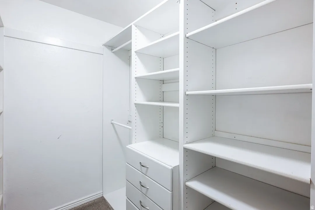 Walk-in closet featuring white built-in shelving, multiple hanging rods, and integrated drawers with chrome hardware