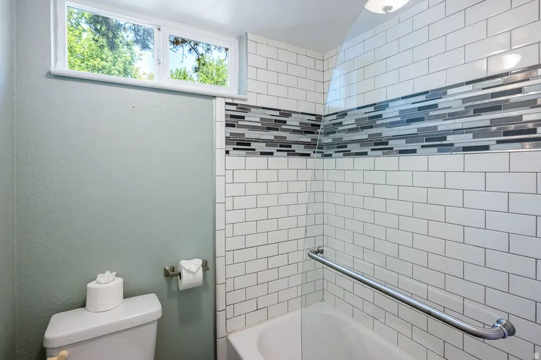 Bathtub and shower combination featuring white subway tile surround with a decorative mosaic accent band