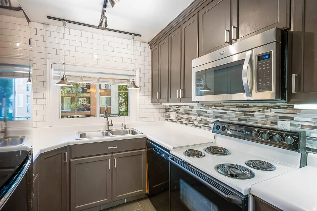 Kitchen featuring dark wood cabinetry, white countertops, a subway tile backsplash, a stainless steel microwave, and a double basin sink with a window overhead