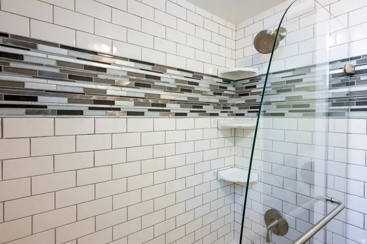 Shower enclosure featuring white subway tile, a decorative glass tile accent band, built-in corner shelves, a glass shower door, and brushed nickel fixtures