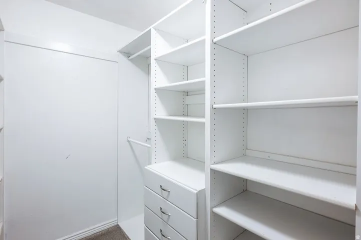 Walk-in closet featuring white built-in shelving, multiple hanging rods, and integrated drawers with chrome hardware