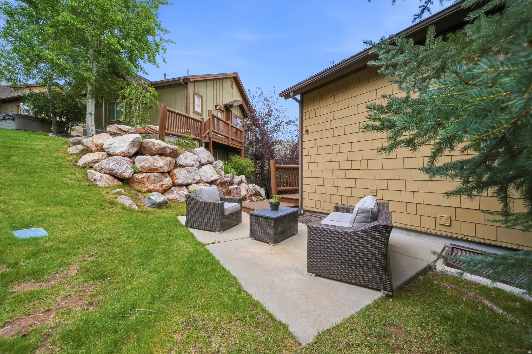 Concrete patio with a rock retaining wall and sloped lawn