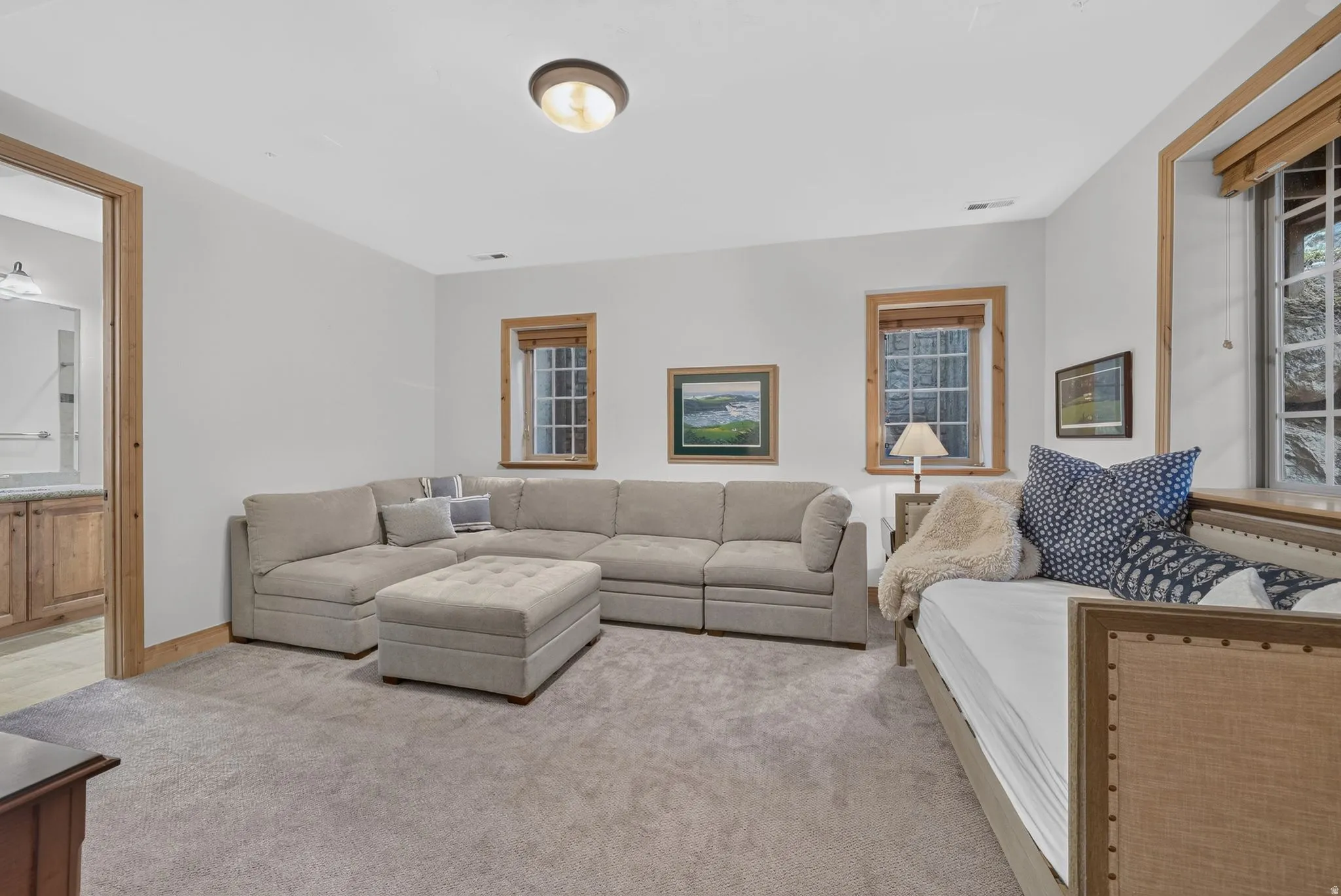 Carpeted recreation room featuring white walls, three windows with natural wood trim, and a flush-mount ceiling light
