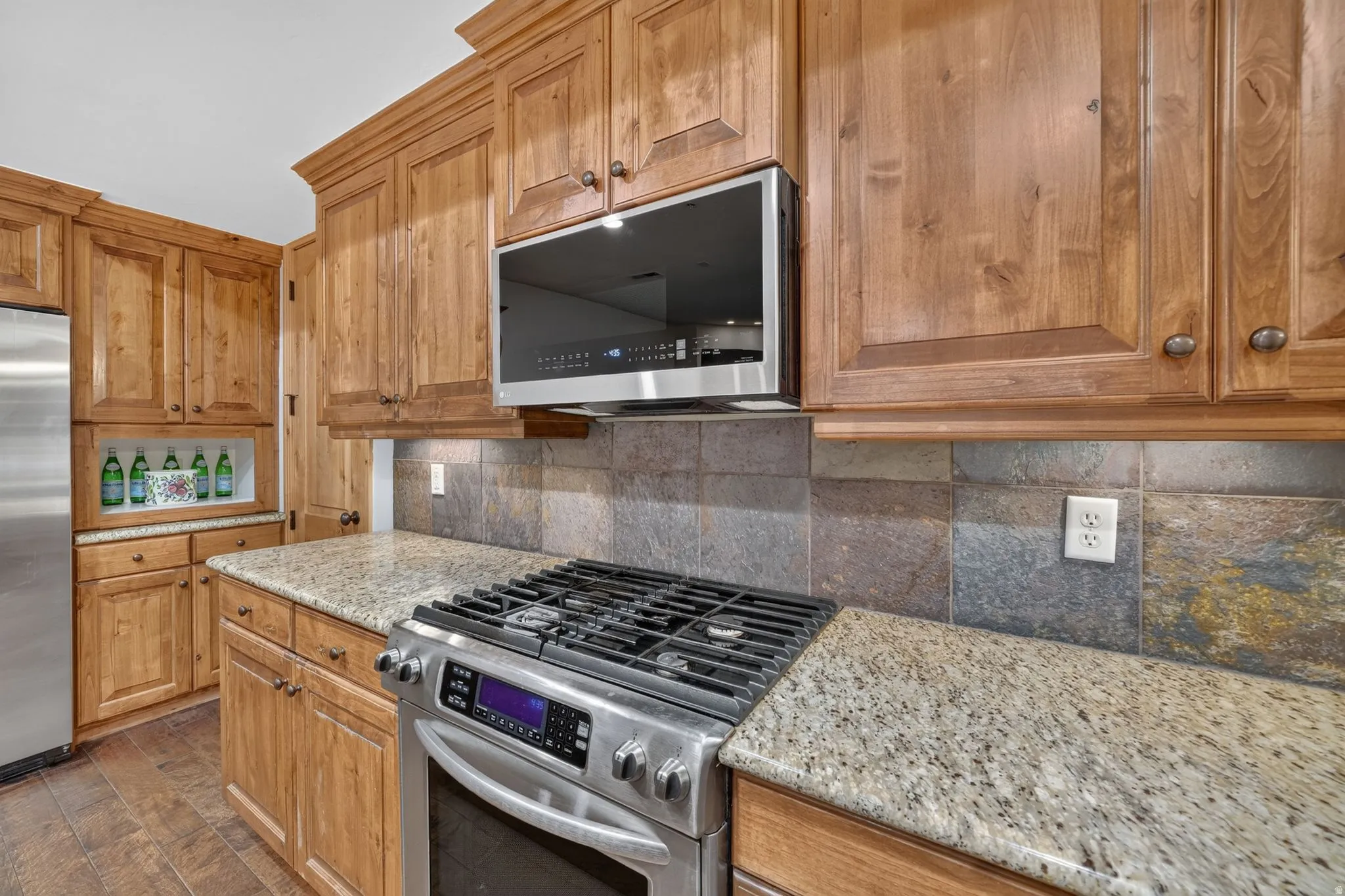Stainless steel oven range with an overhead microwave set against a natural stone tile backsplash