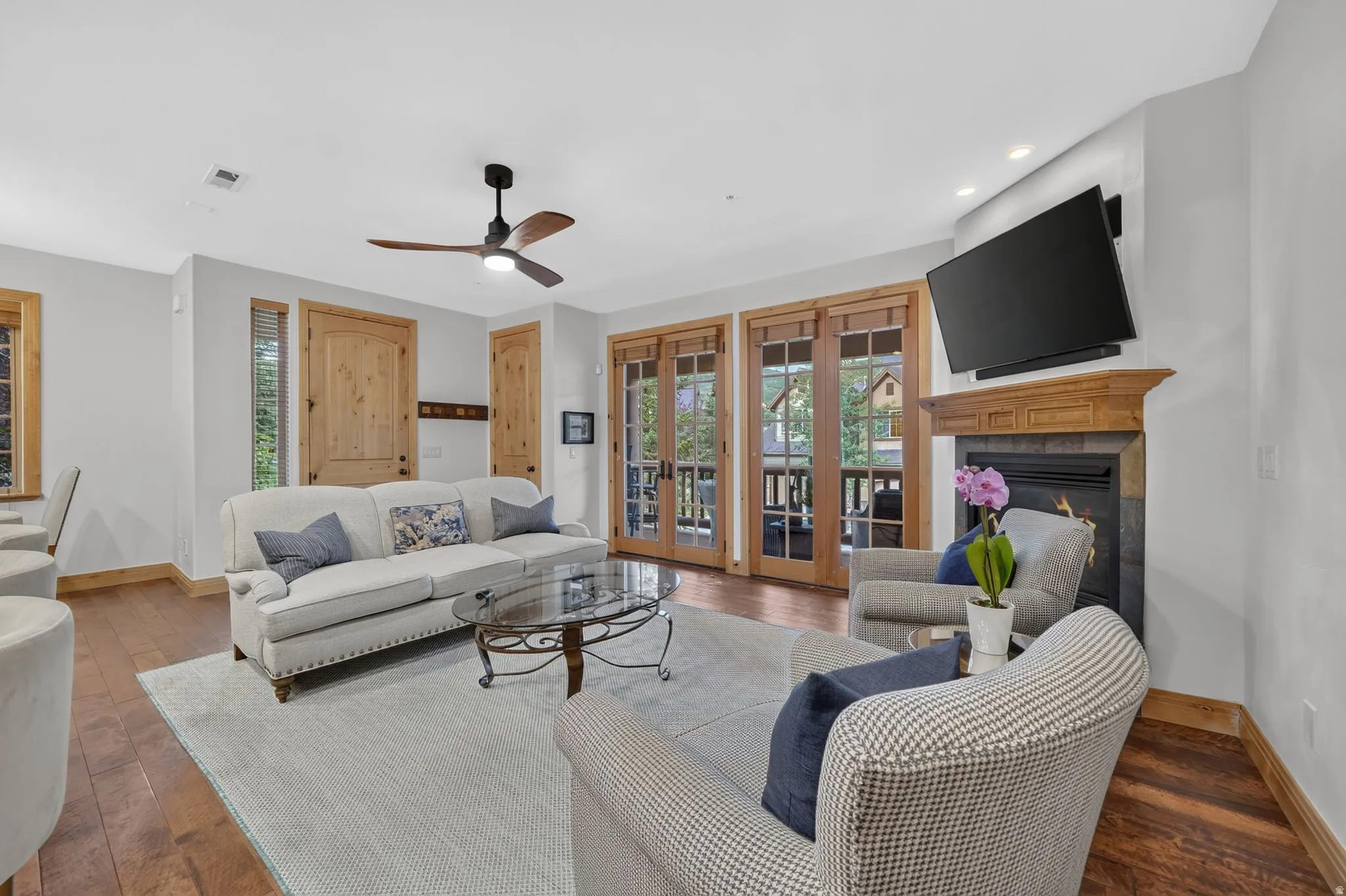 Living area featuring wood-finish flooring, a stone-clad fireplace with a wood mantel, and double French doors opening to an exterior space