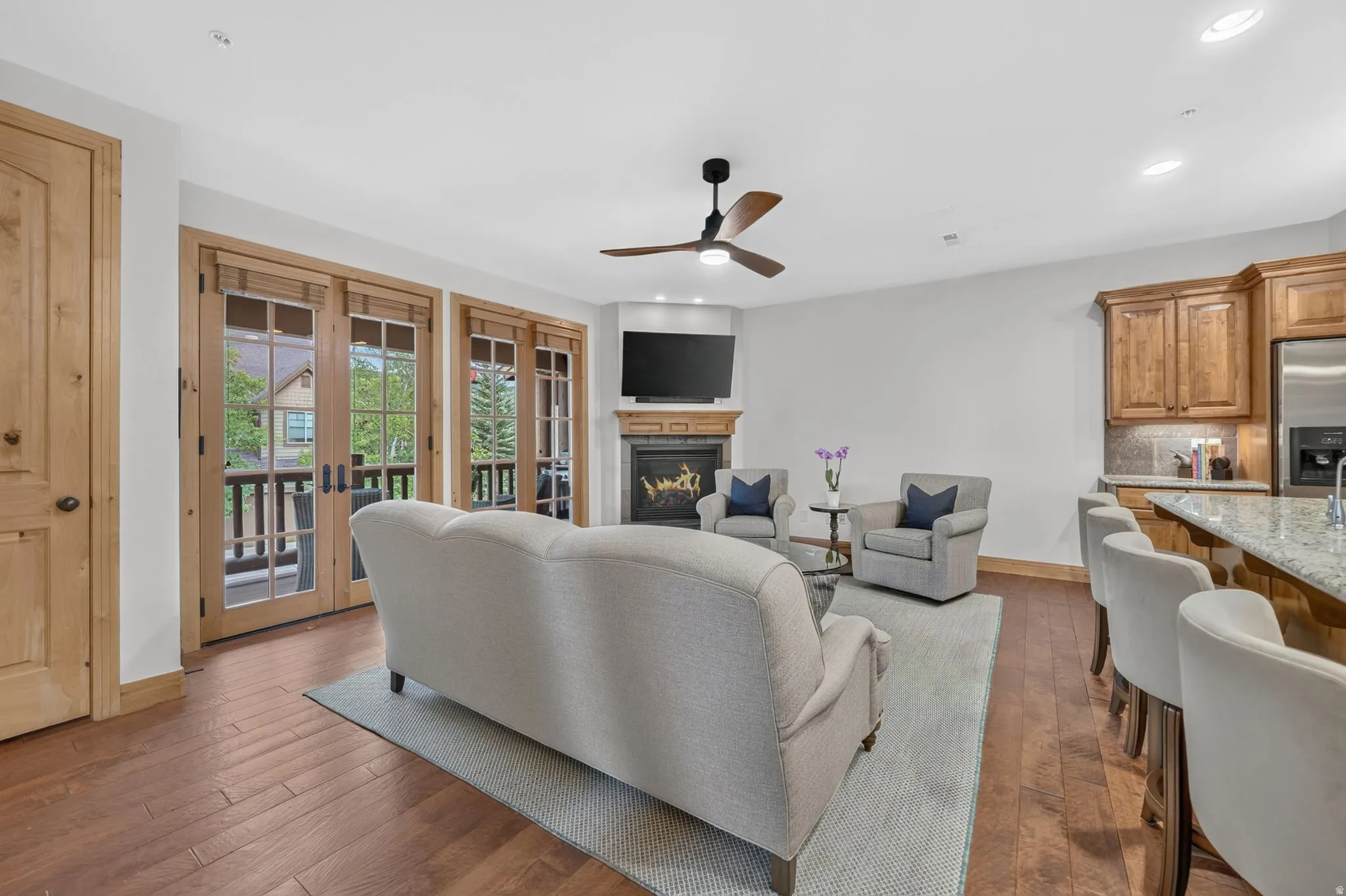 Living area featuring wood-finish flooring, a corner fireplace with a wood mantle, white walls, and a ceiling fan