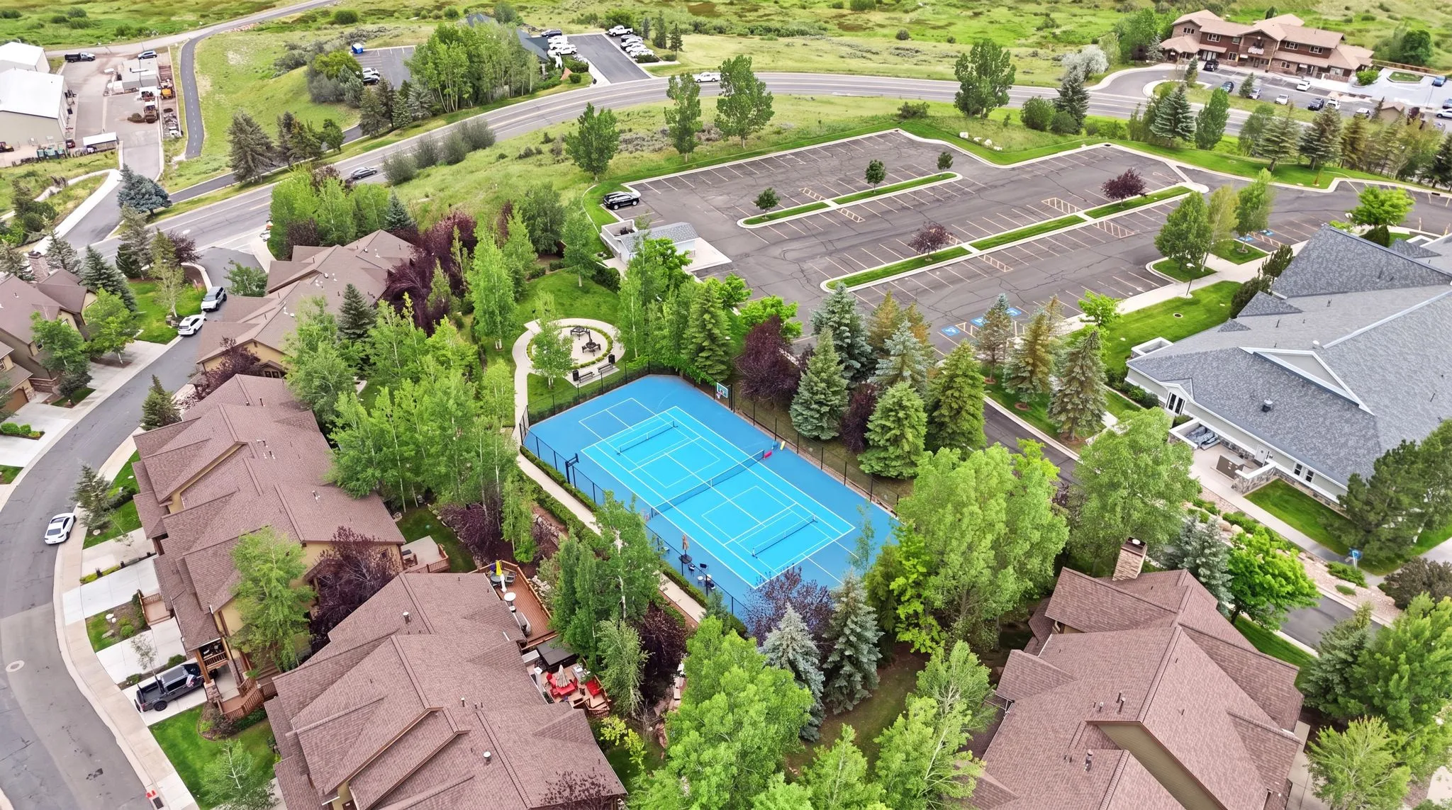 Tennis court surrounded by mature trees, adjacent to residential structures