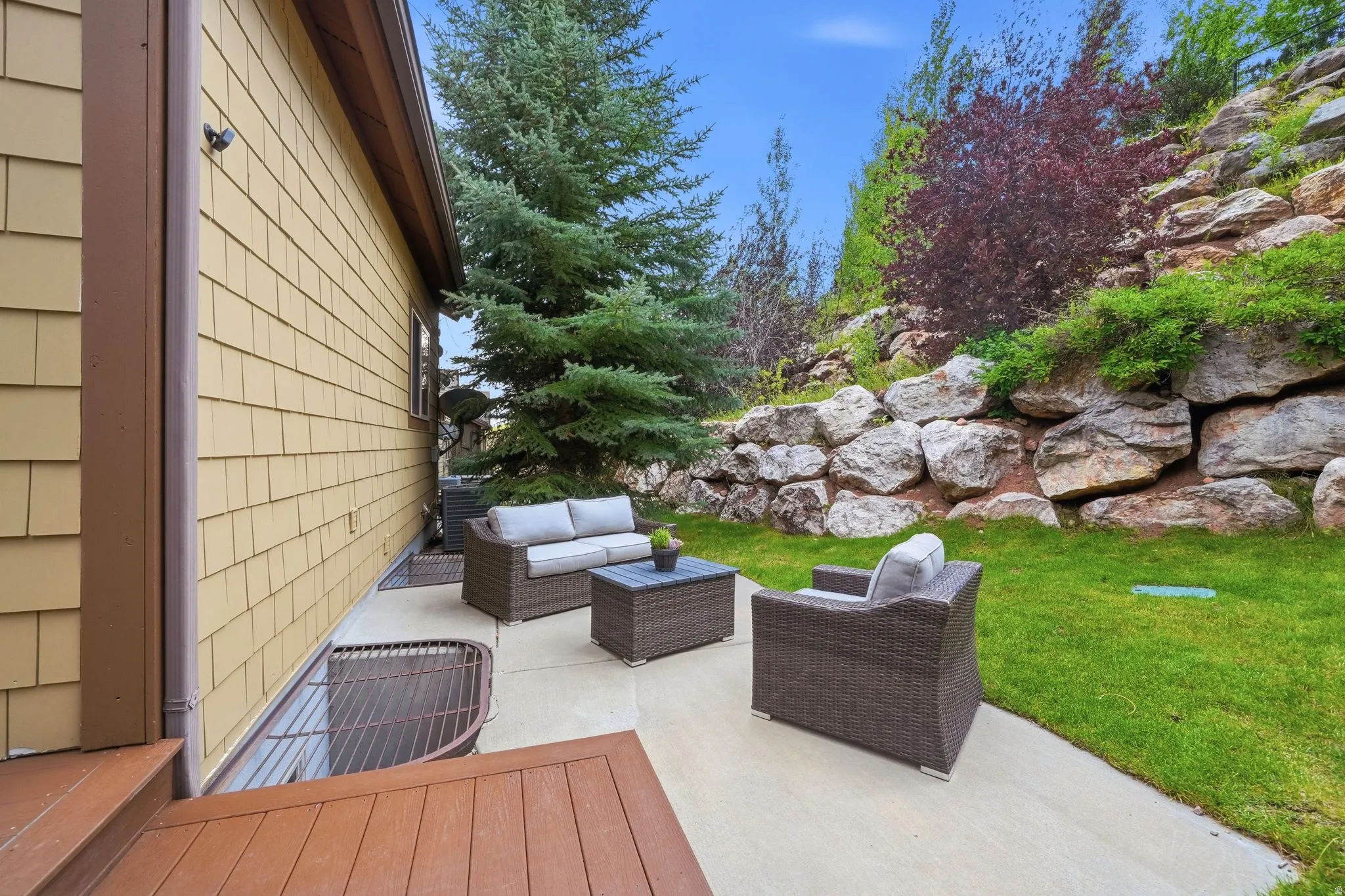 Outdoor patio featuring a concrete surface, a tiered rock retaining wall, and a green lawn area