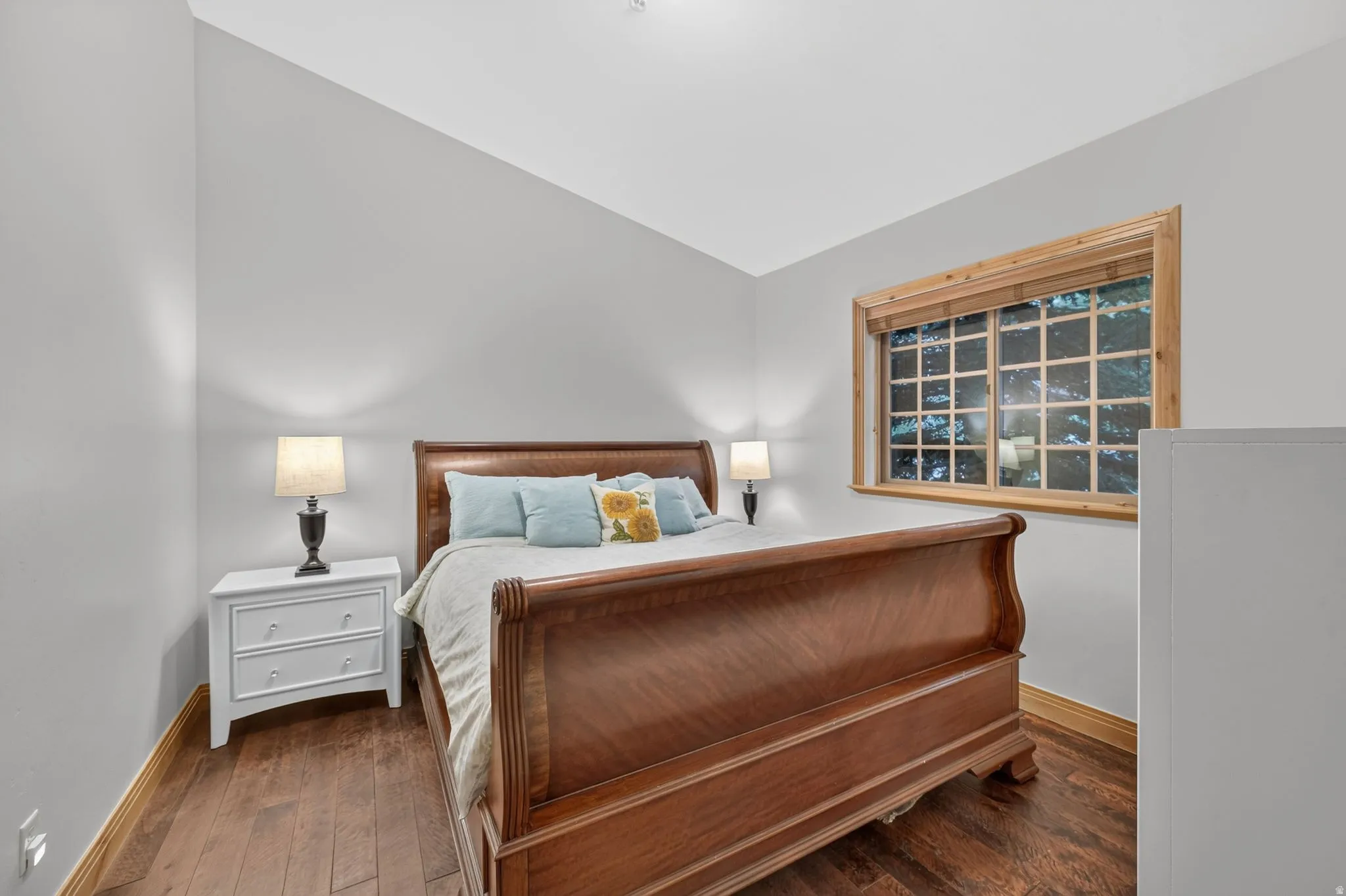 Spacious room featuring wood-finish flooring, a multi-pane window with natural wood trim, and light gray walls