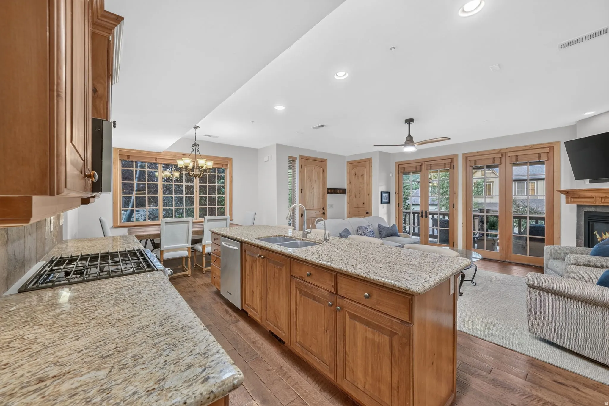 Open-concept living space featuring wood-finish flooring, a kitchen island with stone countertop, stainless steel appliances, and French doors