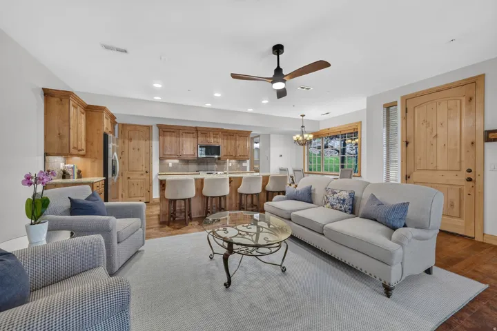 Open-concept living space featuring wood-finish flooring, a ceiling fan with light fixture, and a kitchen with wood cabinetry, a built-in microwave, and an island with counter seating