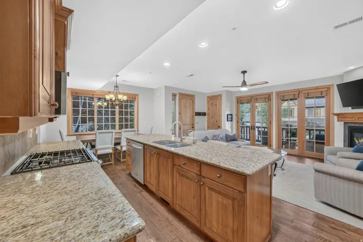 Open-concept living space featuring wood-finish flooring, a kitchen island with stone countertop, stainless steel appliances, and French doors
