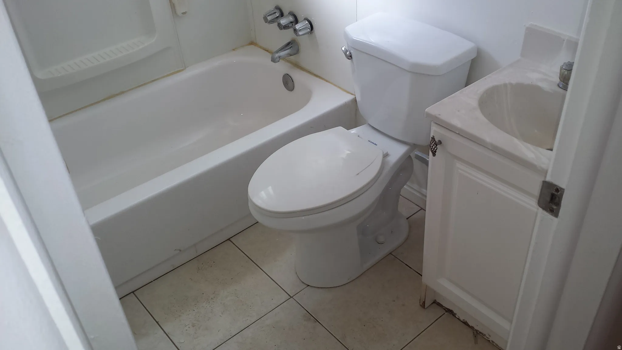 White porcelain bathtub and toilet with a single vanity featuring a built-in sink and white cabinetry