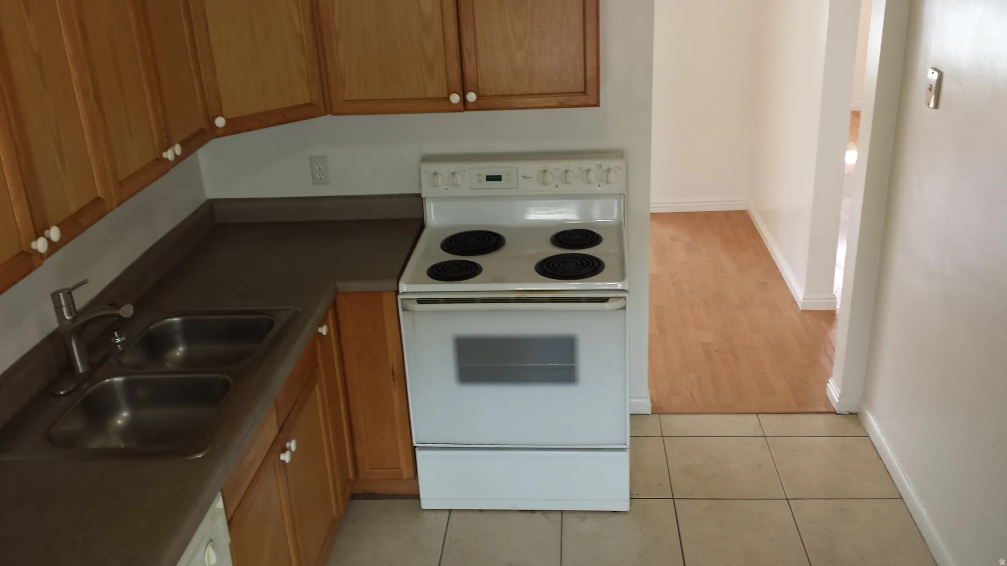 Kitchen area featuring wood-finish cabinetry, a dual basin stainless steel sink, and a white electric range