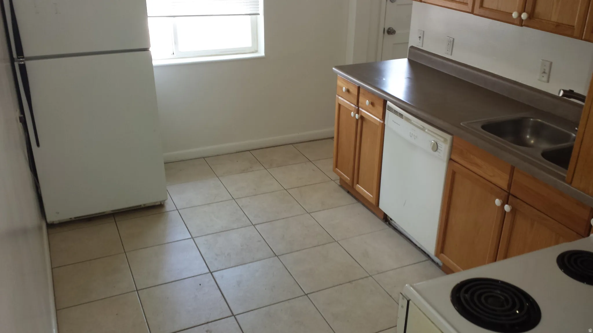 Kitchen featuring tile flooring, wood cabinetry, a double basin stainless steel sink, and a white dishwasher