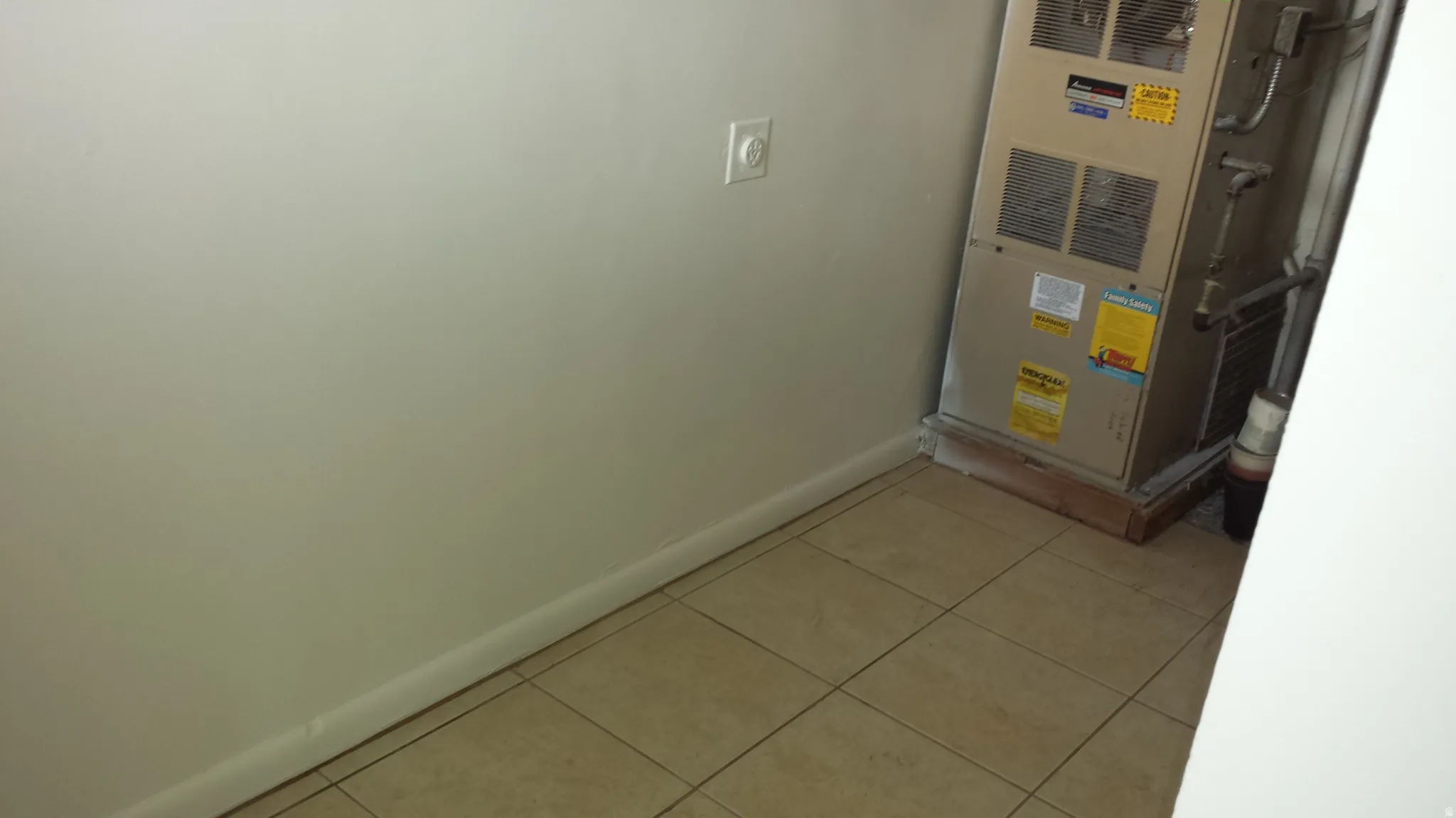 HVAC unit on a raised wooden platform, featuring tiled flooring, a light-colored wall, and white baseboards
