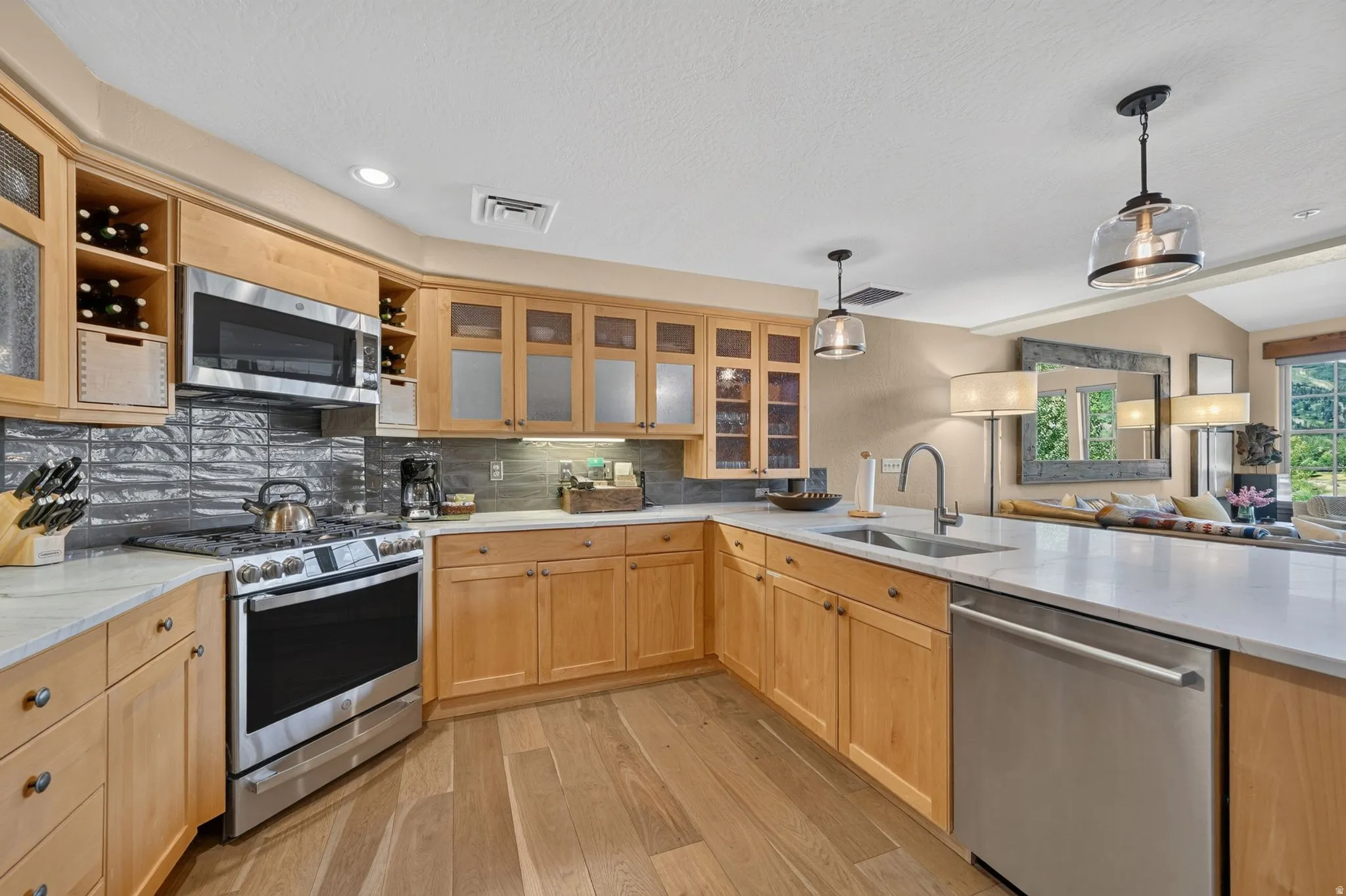 Well-appointed kitchen featuring light wood cabinetry, stainless steel appliances, a white countertop, and a gray tile backsplash