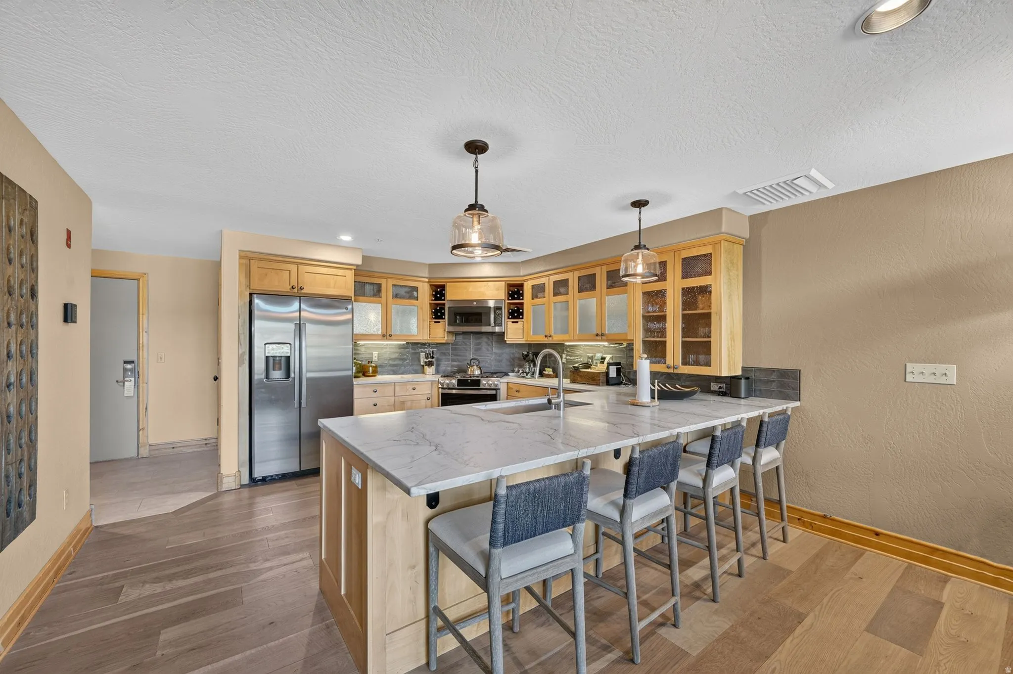 Kitchen featuring a substantial island with seating, stainless steel appliances, light wood-finish cabinetry, and pendant lighting