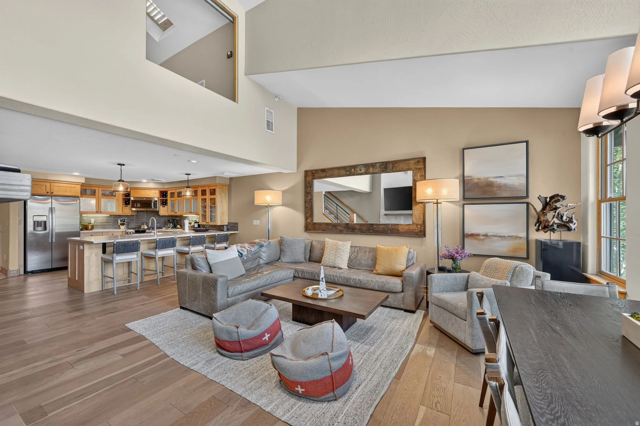 Open-concept living space featuring wood-finish flooring, a kitchen island with seating, stainless steel appliances, and a two-story ceiling with a visible upper-level hallway