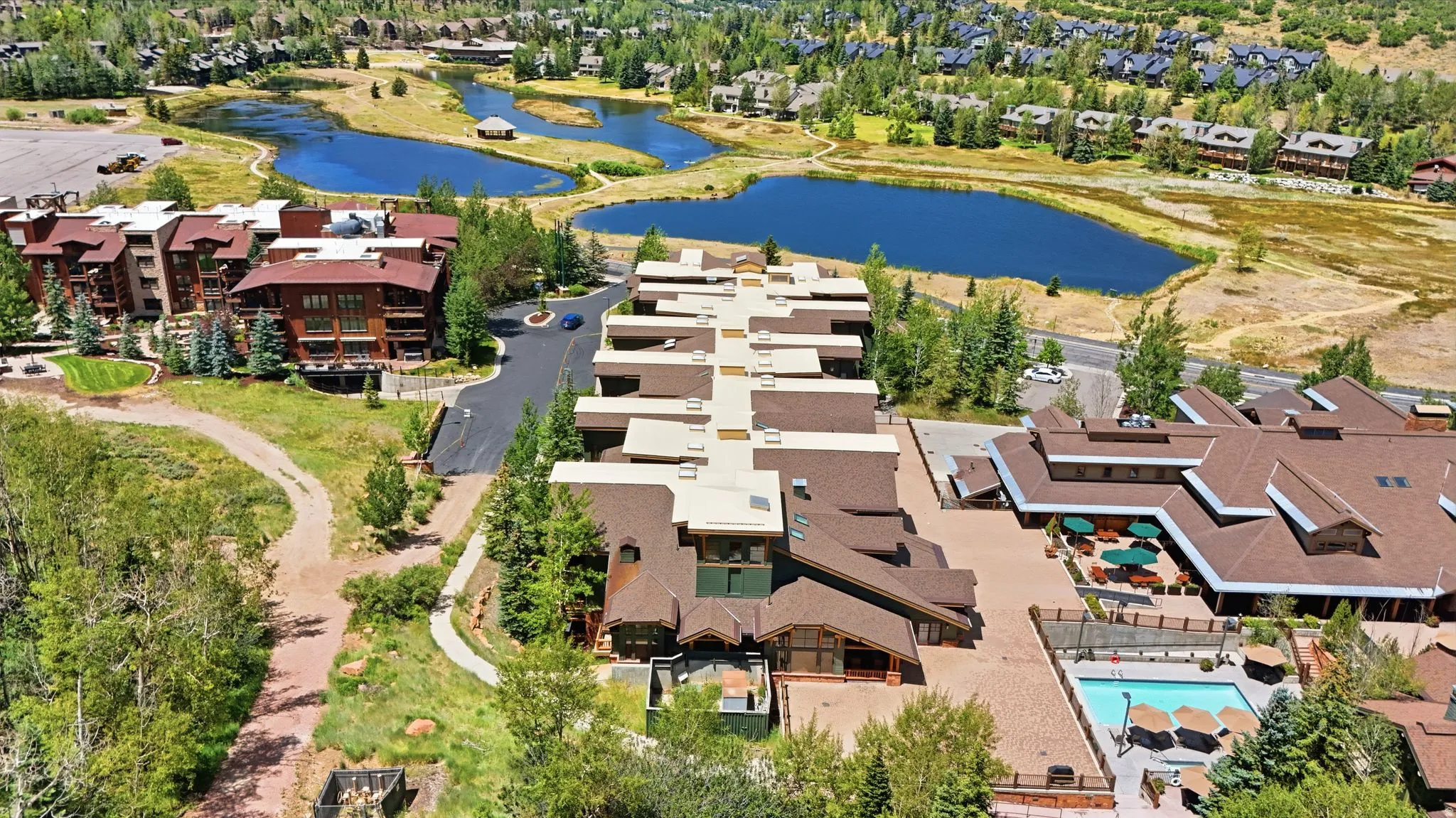 Expansive resort property featuring multiple buildings with sloped roofs, an outdoor swimming pool with lounge seating, and varied landscaping