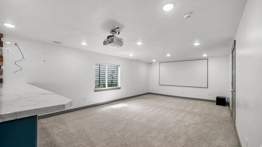 Entertainment room featuring a ceiling-mounted projector, large projection screen, recessed lighting, and light-tone carpet flooring