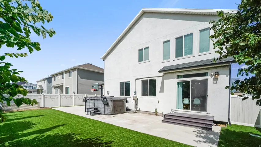 Expansive backyard featuring a manicured lawn, concrete patio, and white privacy fencing