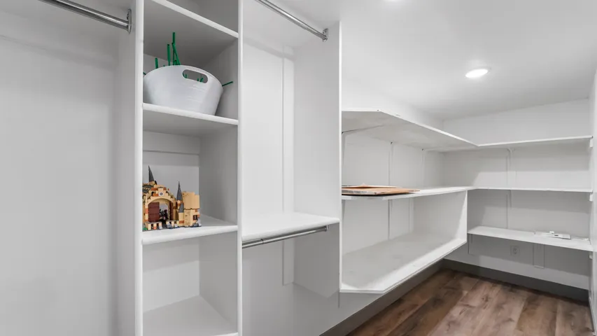 Spacious walk-in closet featuring white built-in shelving, chrome hanging rods, recessed lighting, and wood-finish flooring