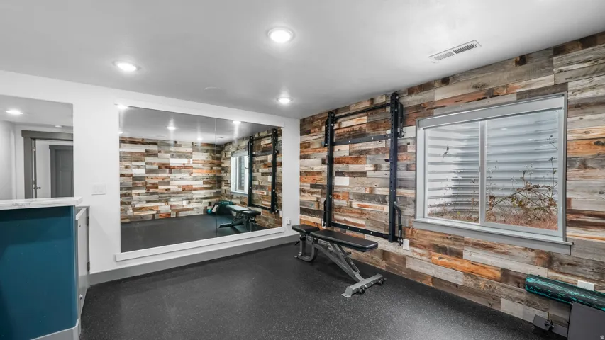 Dedicated fitness space featuring a full wall mirror, wood-finish accent wall, recessed lighting, and durable rubber flooring