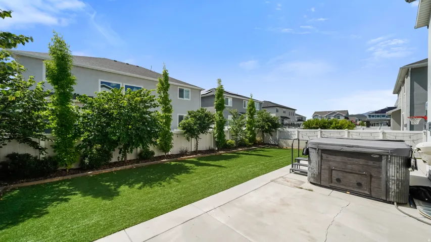 Spacious backyard featuring artificial turf, mature perimeter trees, a concrete patio, and swim spa