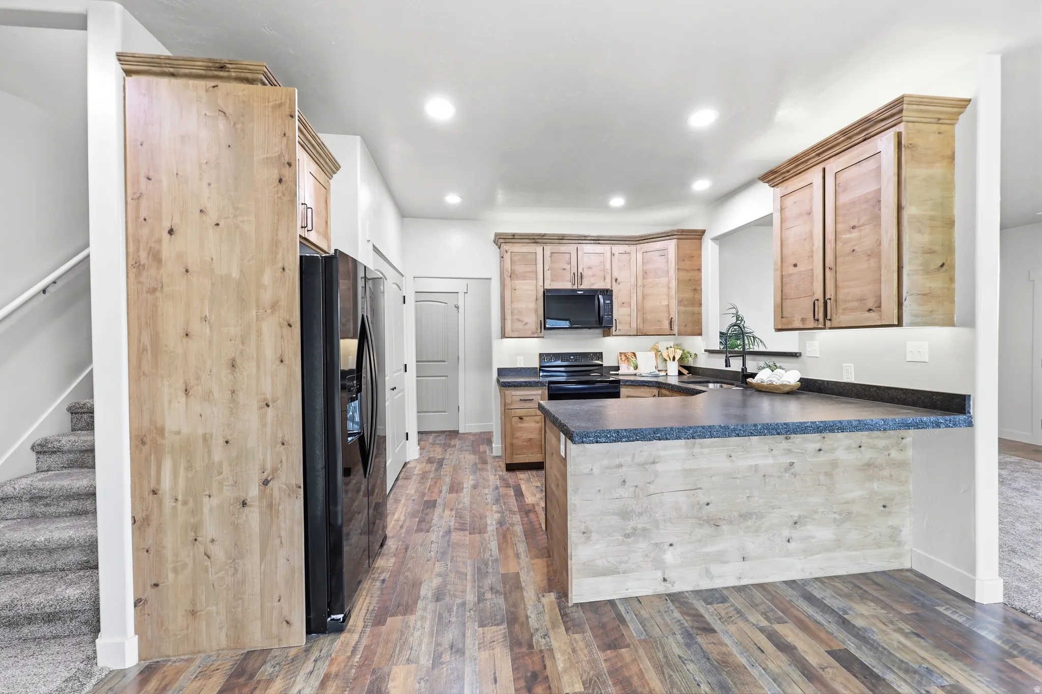 Kitchen featuring wood-finish flooring, custom wood cabinetry, dark countertops, and black appliances