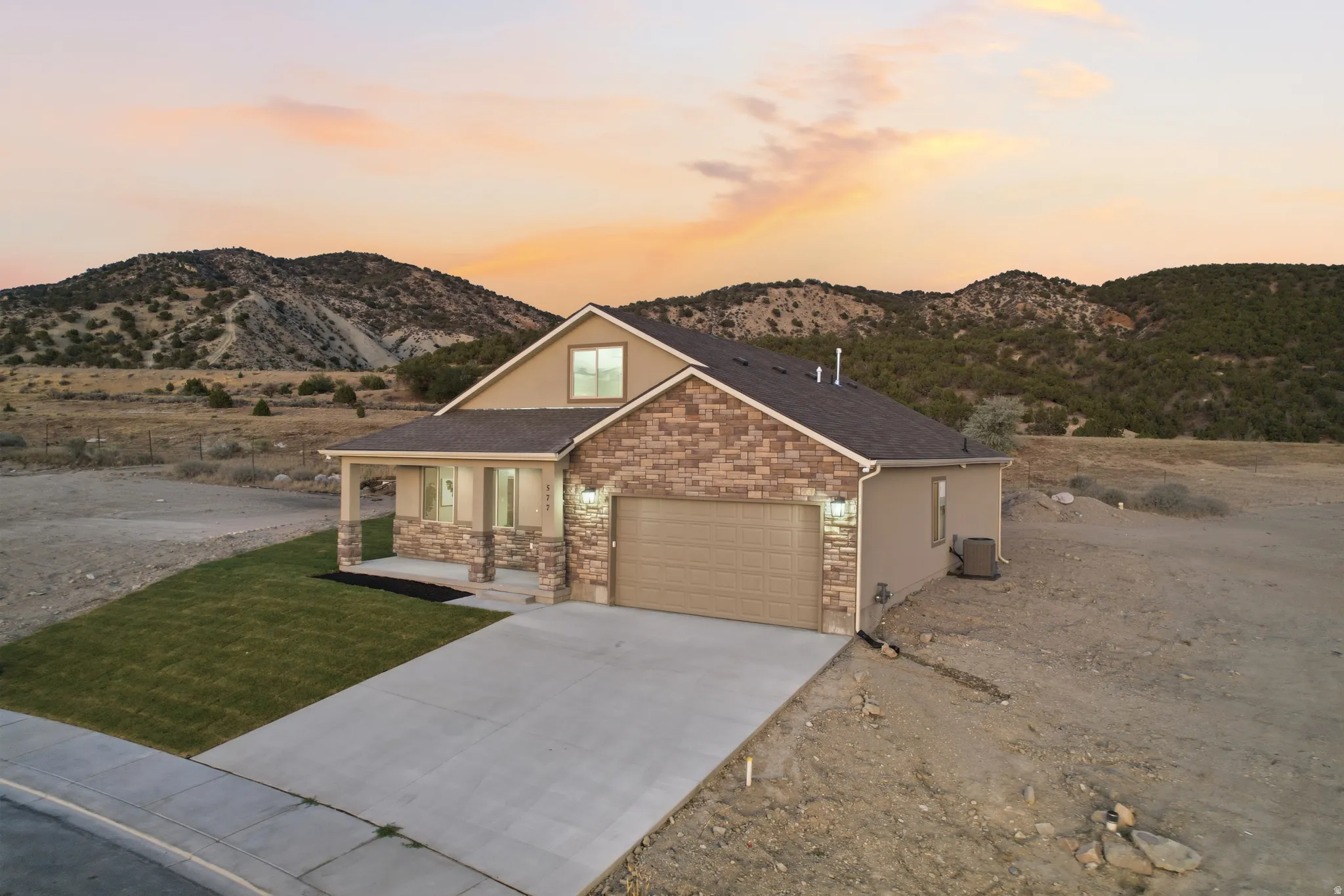 Contemporary residence featuring a two-car garage, partial stone facade, covered porch with columns, and a manicured front lawn