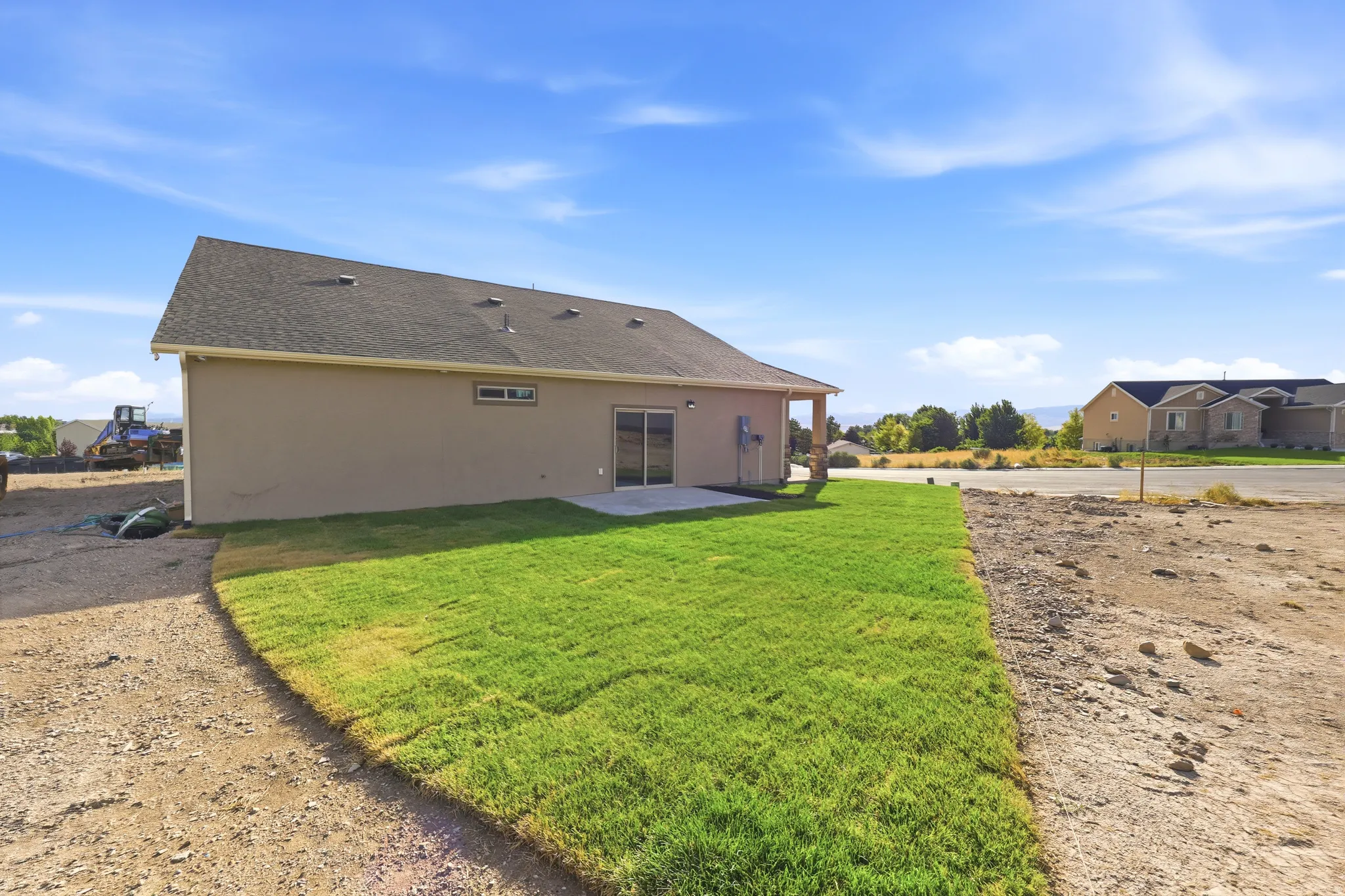 Stucco exterior featuring a dark shingled roof, a rear patio, and a newly sodded lawn