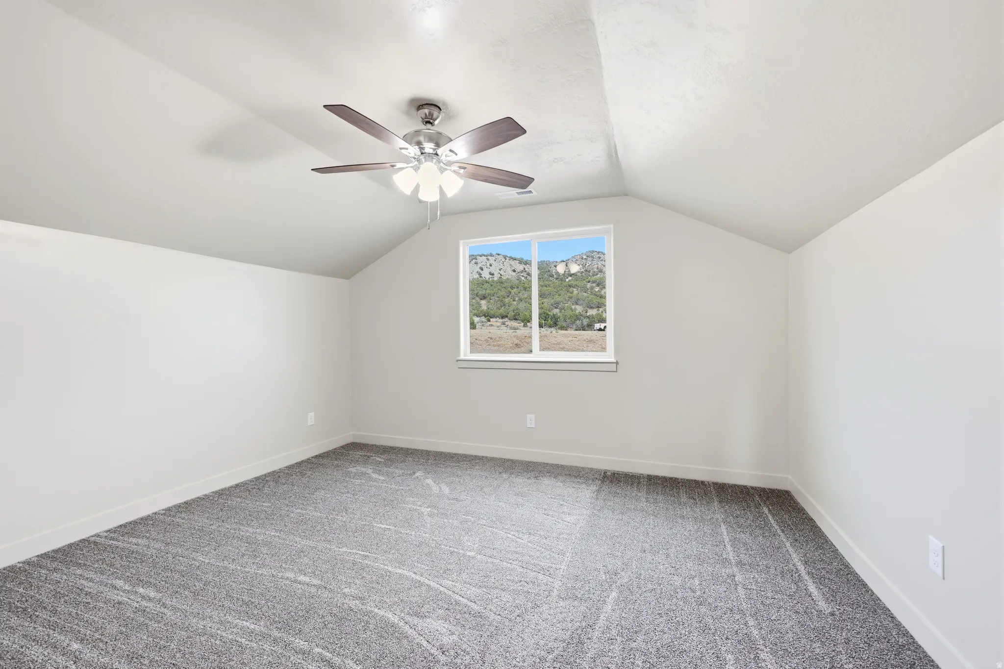Spacious interior featuring vaulted ceilings, a contemporary ceiling fan with integrated lighting, and plush grey carpeting