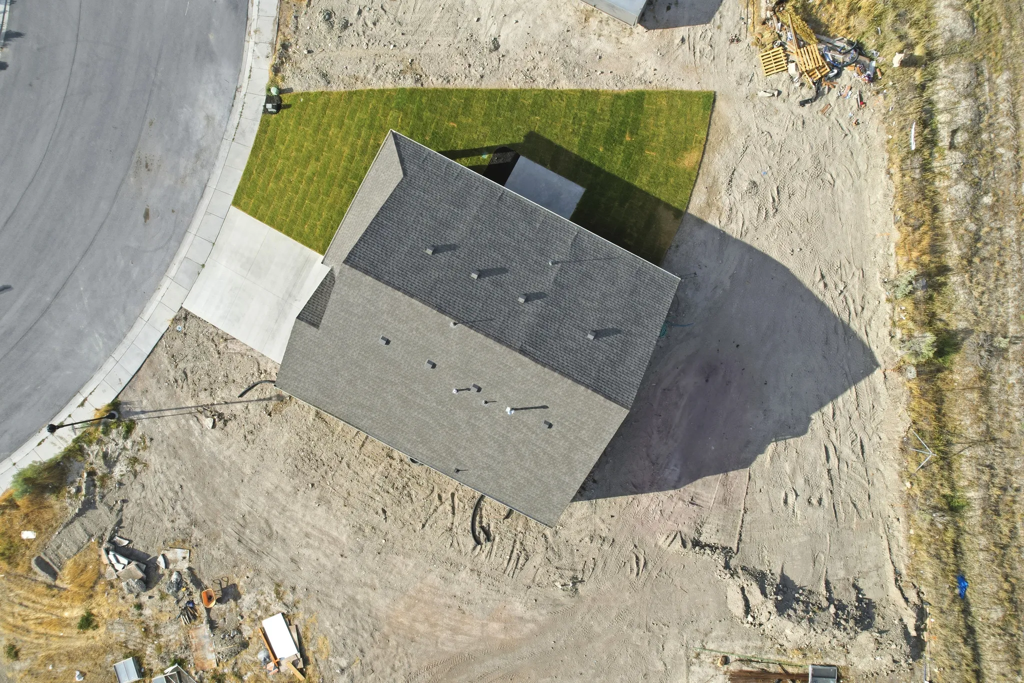 Newly constructed residence featuring a shingled roof, a paved driveway, and a partially grassed lot