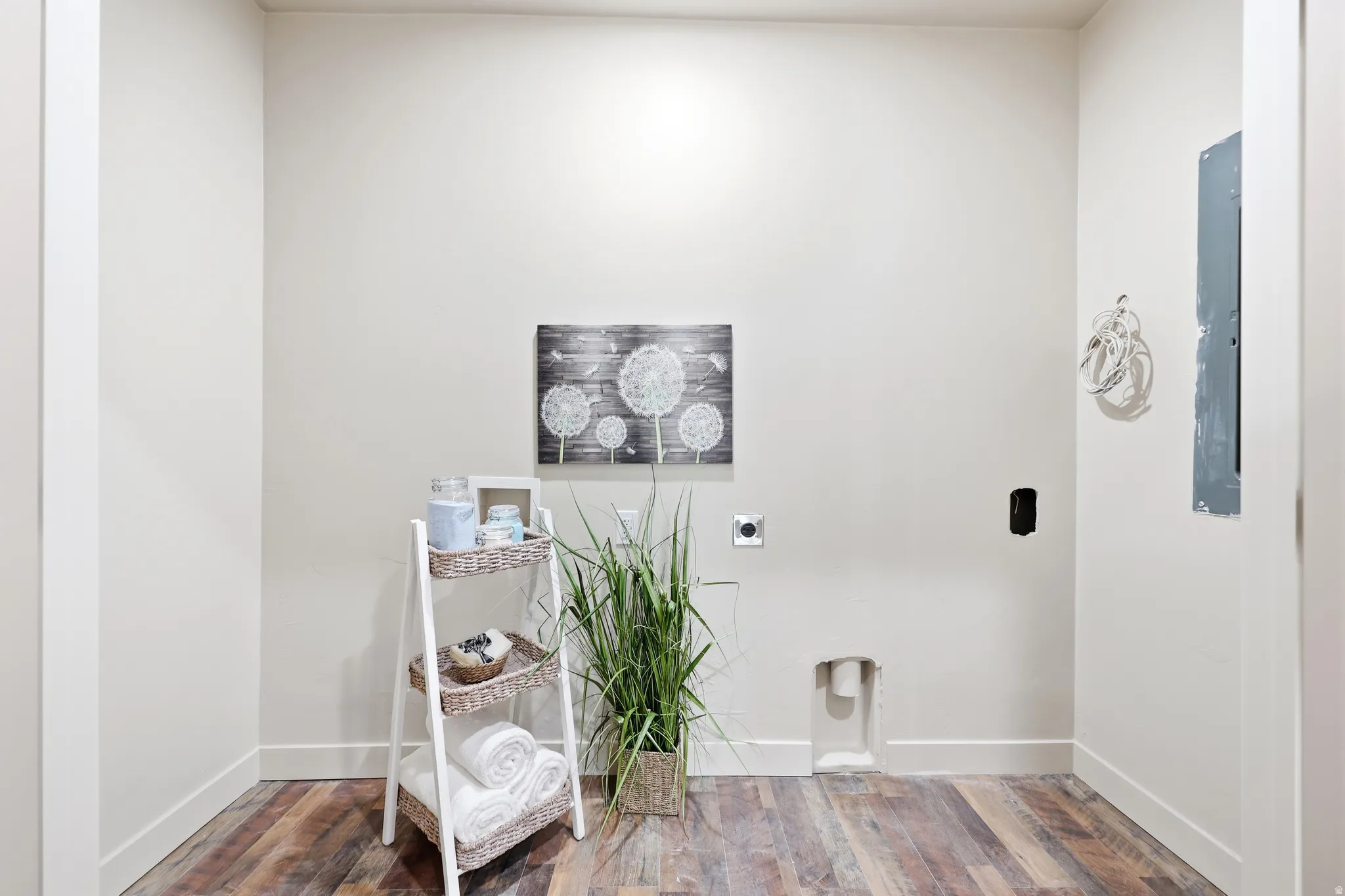 Laundry area featuring wood-finish flooring, light neutral wall paint, and white baseboards