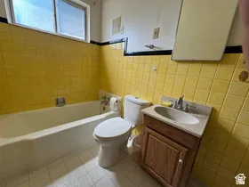 Bathroom featuring yellow square tile walls, a white bathtub, a toilet, a vanity with a white basin sink, and a window providing natural light