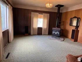 Spacious room featuring wood paneling, multiple windows with natural light, a central wood-burning stove on a stone hearth, and an overhead chandelier light fixture
