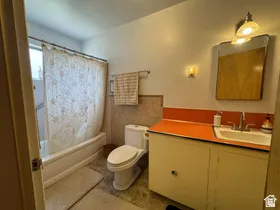 Bathroom featuring a built-in tub with shower, single vanity with orange countertop, chrome faucet, and wall-mounted mirror
