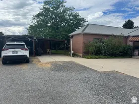 Brick exterior with a gray shingle roof, accompanied by a gravel driveway and partial concrete surfacing
