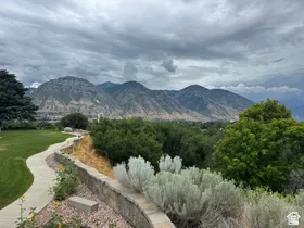 Mountain backdrop with expansive landscaping, stone retaining walls, a winding paved pathway, and mature trees and shrubs