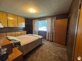 Bedroom featuring integrated wood cabinetry, a built-in dresser, a window with patterned curtains, a ceiling light fixture, and textured ceiling panels