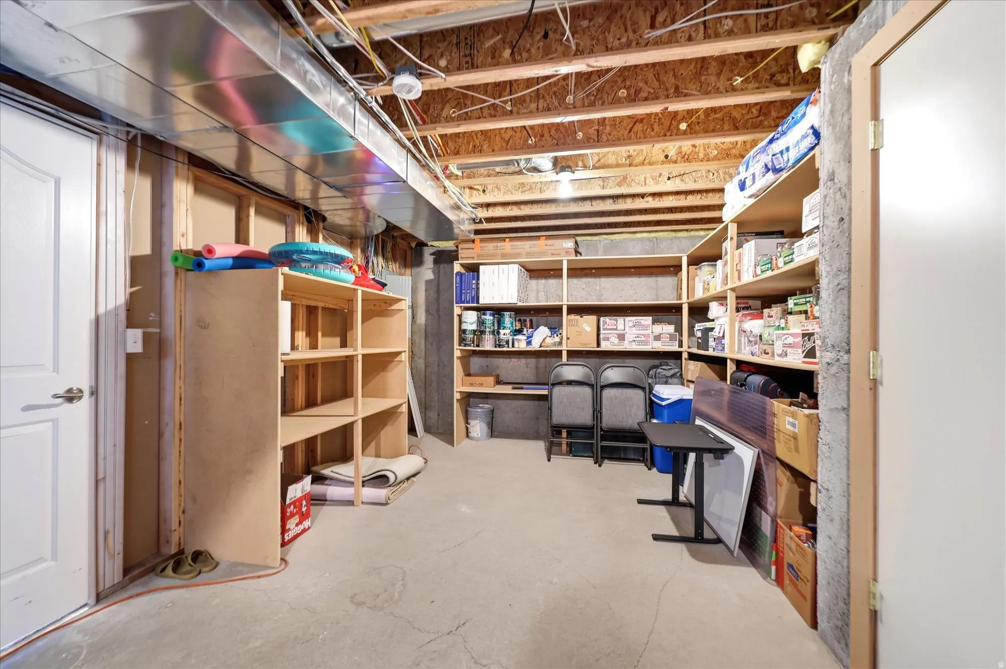 Unfinished basement area featuring exposed ceiling joists, concrete flooring, built-in shelving, and utility access
