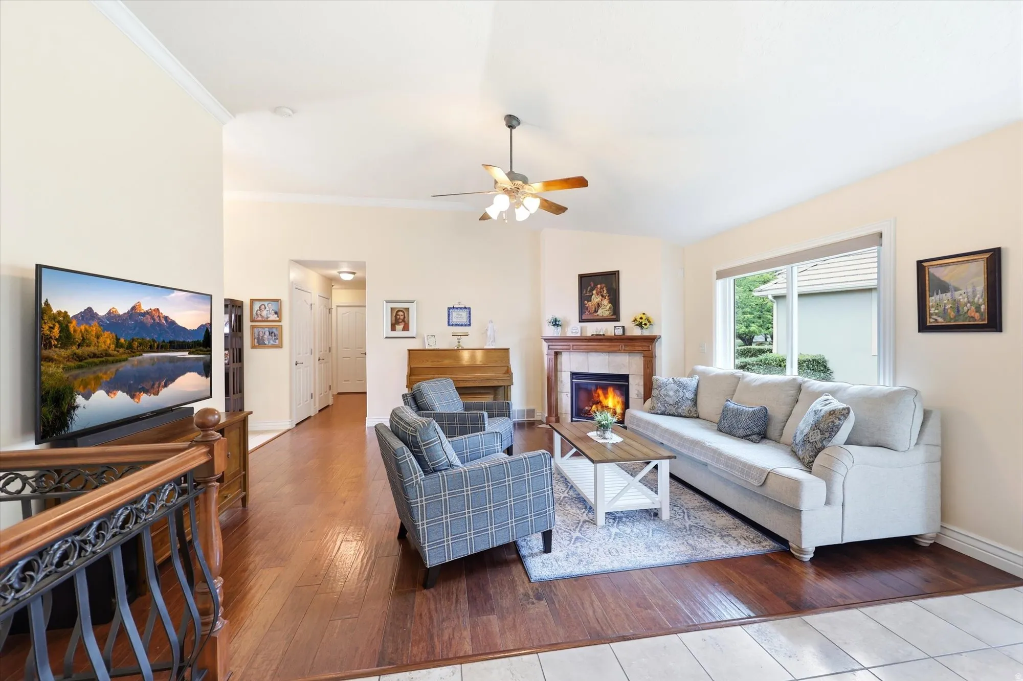 Spacious living area featuring high vaulted ceilings, rich wood-finish flooring, a ceiling fan, and a corner fireplace with a wood mantle and tiled surround
