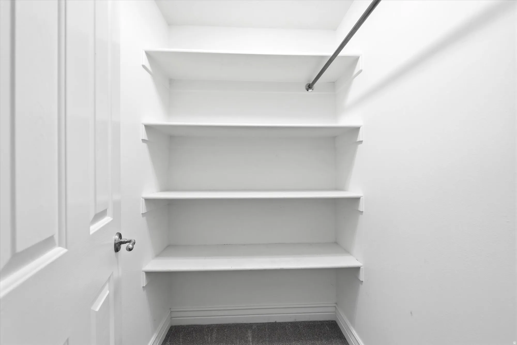 Walk-in closet with four white shelving units, a dark metal hanging rod, white baseboards, and dark gray flooring