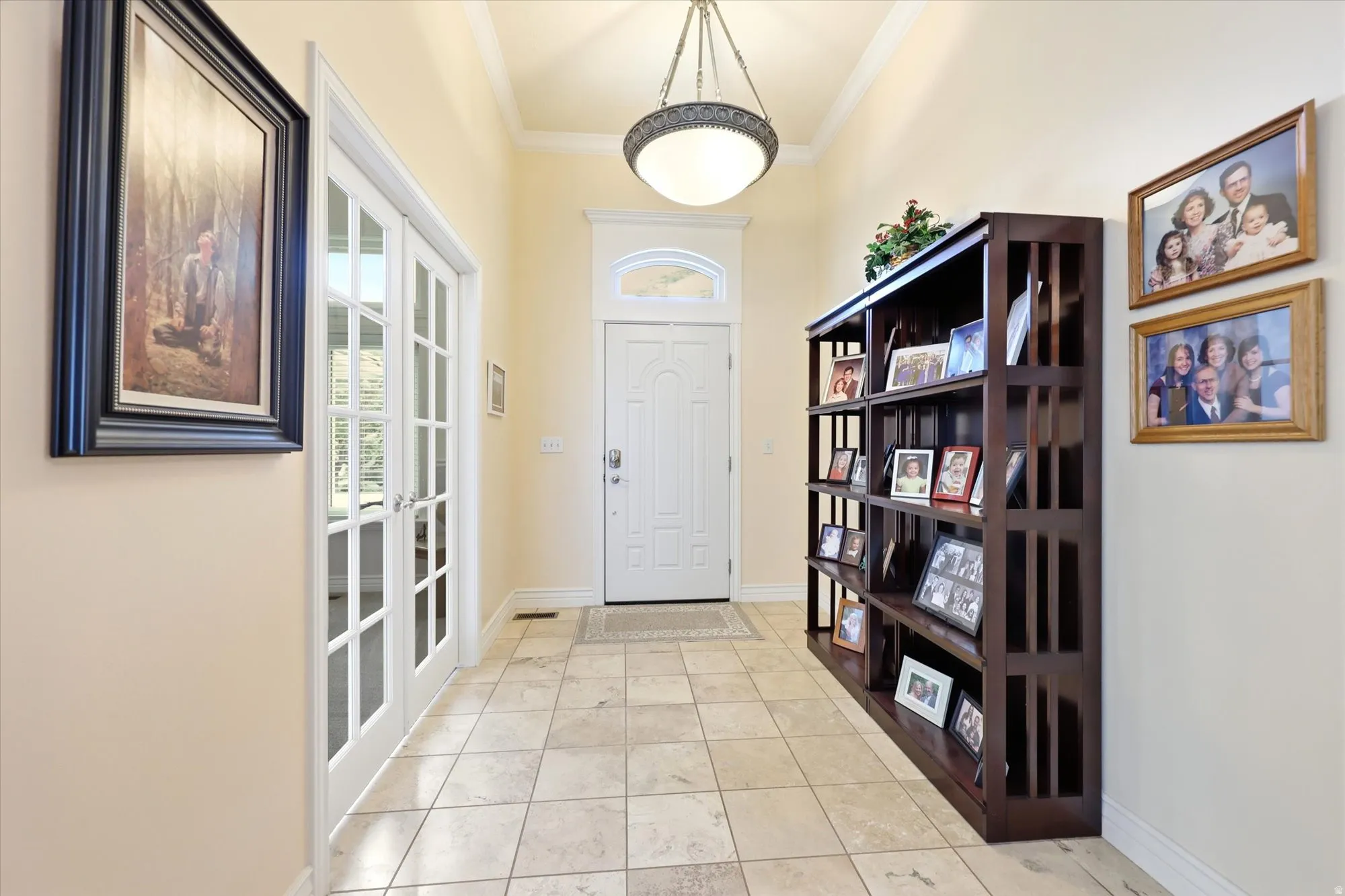 Entryway featuring light-toned tile flooring, a white paneled front door with an arched transom window, and a decorative overhead light fixture