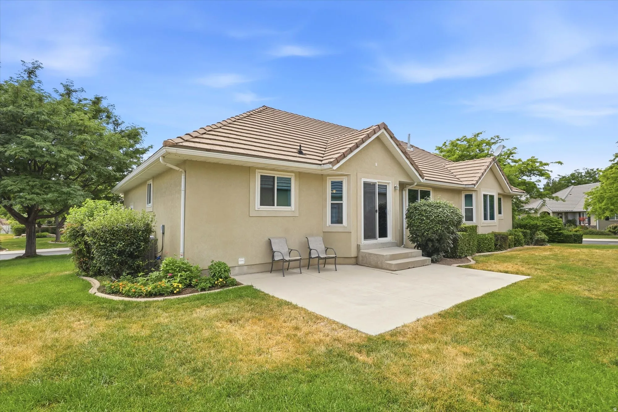 Rear exterior featuring a concrete patio, sliding glass door access, stucco siding, a tiled roof, and mature perimeter landscaping