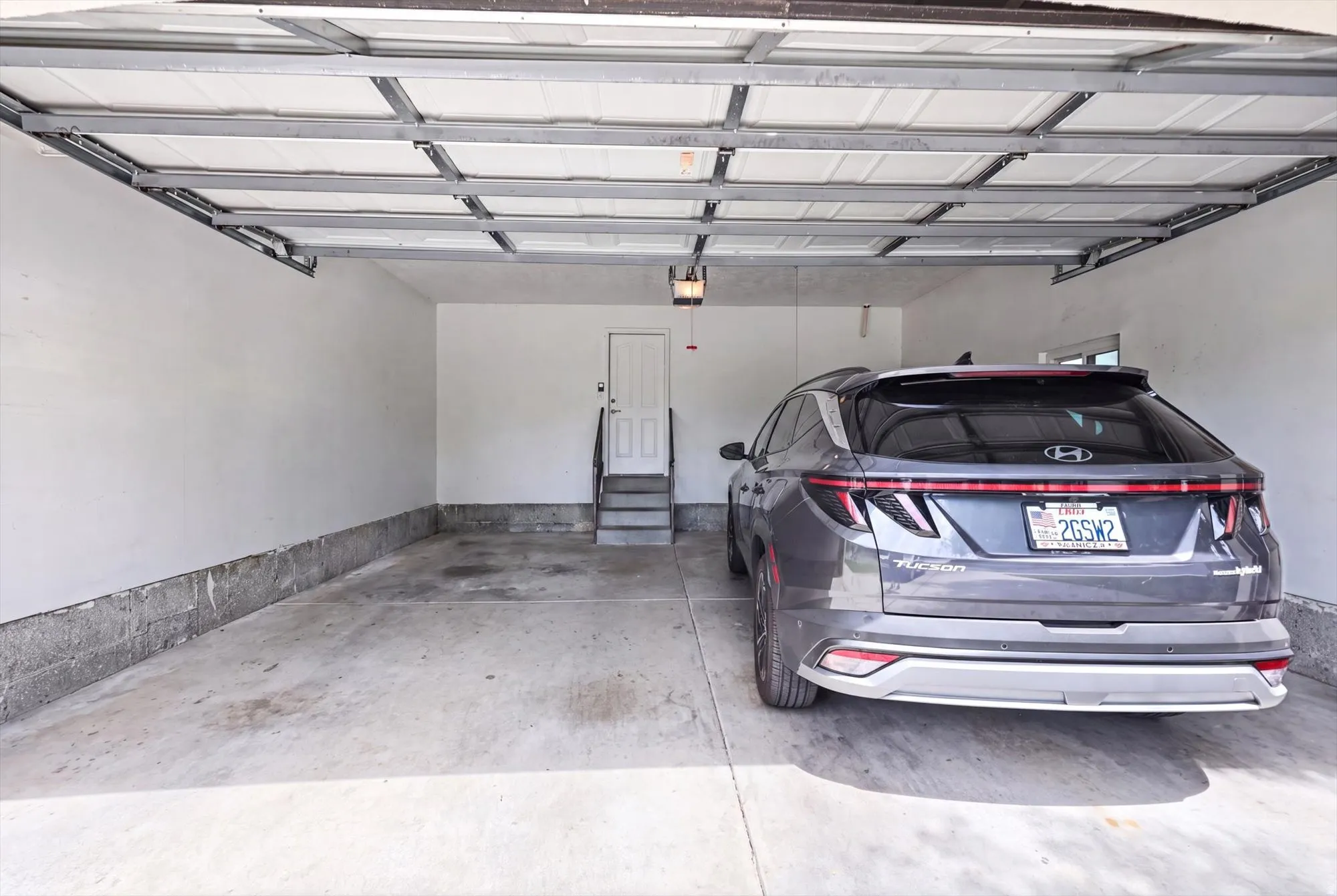 Attached garage with concrete flooring, finished drywall, and a white interior door with steps