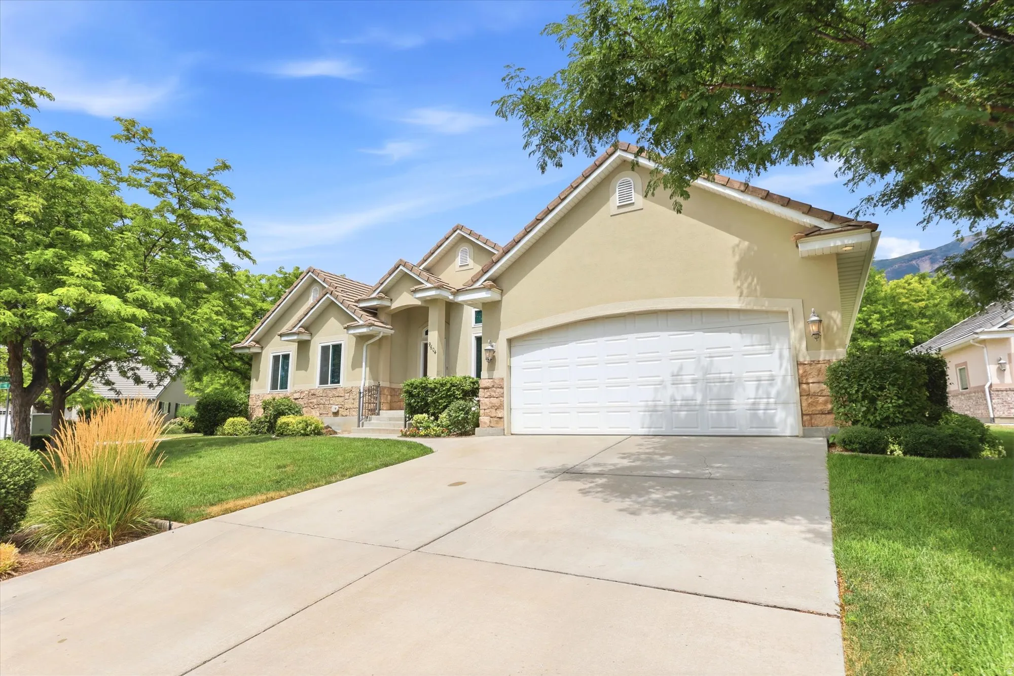 Stucco exterior with stone accents, a tile roof, an arched garage door, and a concrete driveway