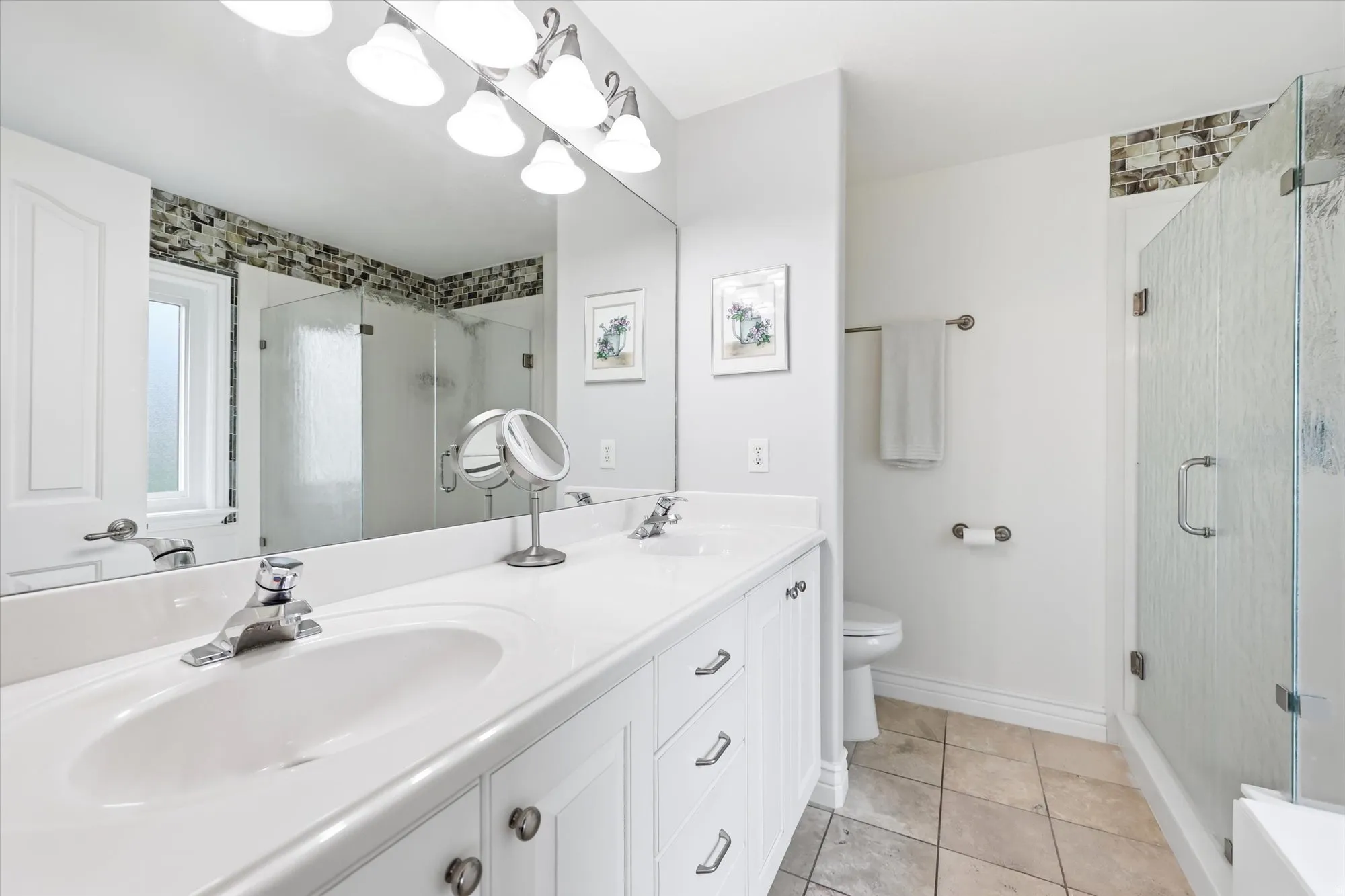 Attached to the primary bedroom. Double vanity with integrated sinks, white cabinetry, and polished chrome fixtures