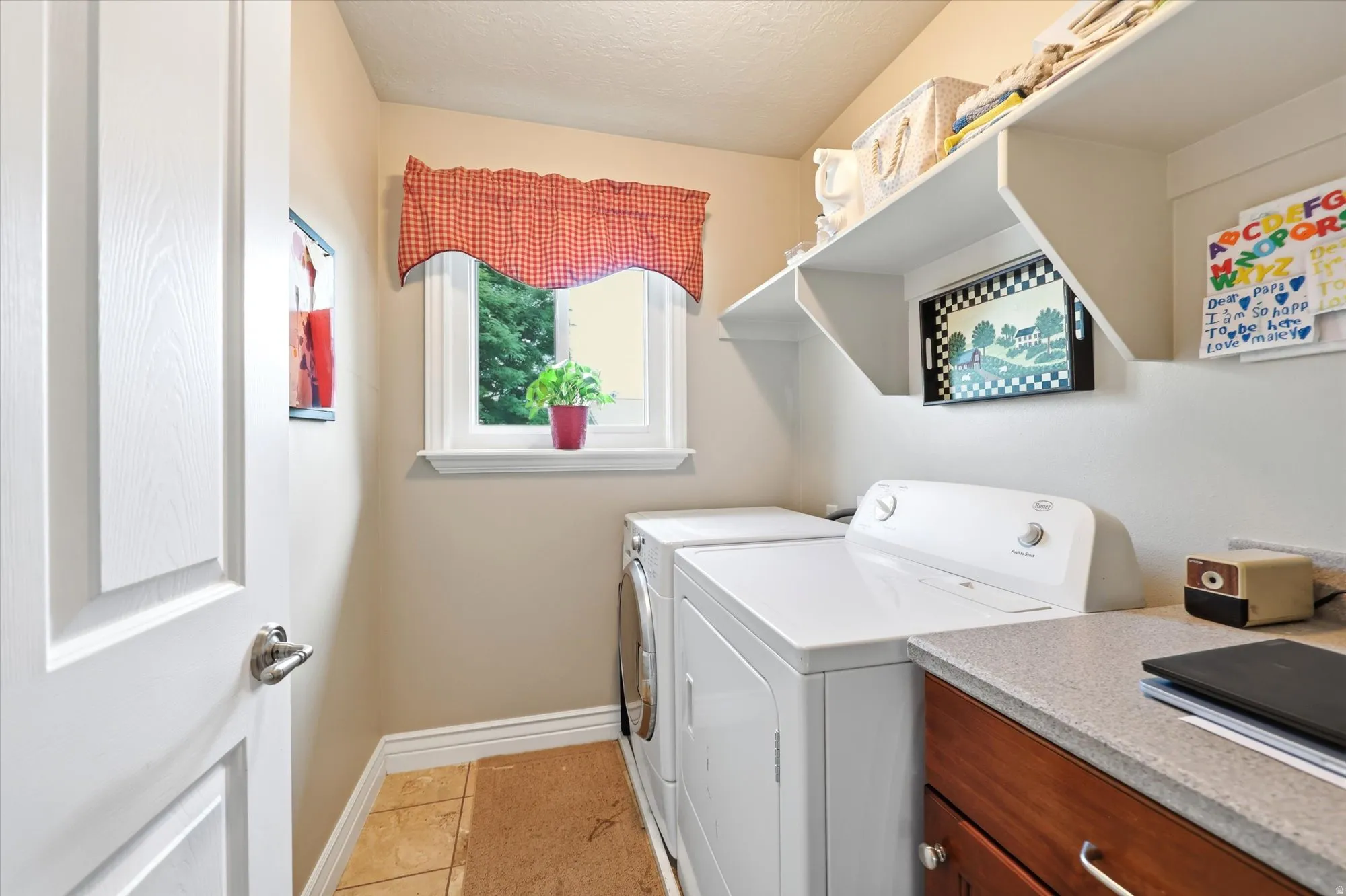 Laundry area featuring white appliances, a window with natural light, tiled flooring, built-in shelving, and a countertop with wood-finish cabinetry